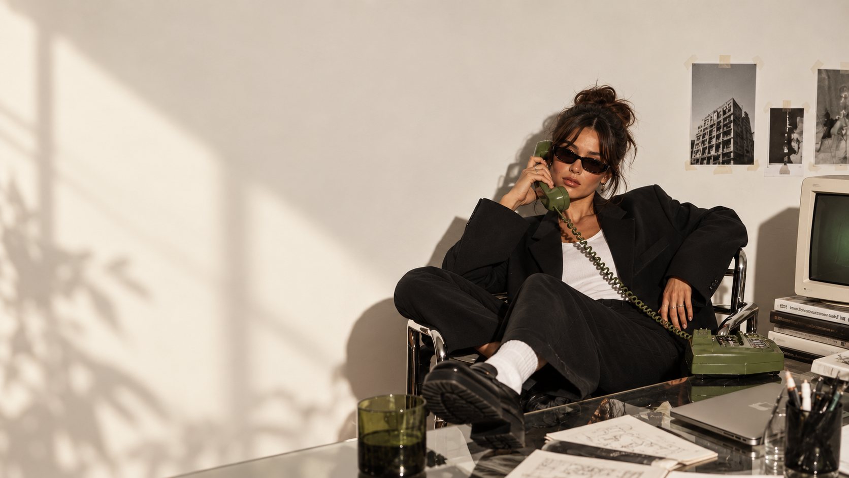 A woman in a black suit on a green rotary phone, leaning back at a desk